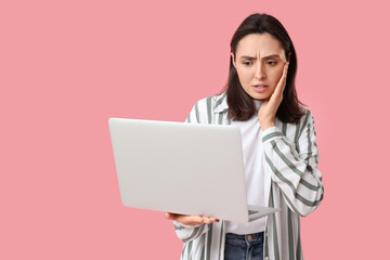 Wall Mural - Confused young woman with laptop on pink background