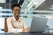 © Liubomir - Confident businesswoman wearing glasses and working on laptop in a modern office environment. Professional setting with clear glass walls and contemporary decor.