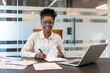 © Liubomir - Confident businesswoman in modern office sitting at her desk with a laptop and documents, smiling while working.