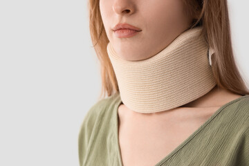 Poster - Injured young woman with cervical collar after accident on light background, closeup