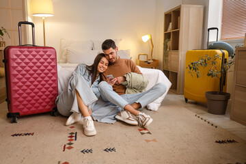 Poster - Young couple of tourists using mobile phone in hotel room at night