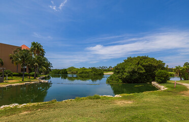 Wall Mural - Stunning tropical scenery featuring a lake and a golf course set against a backdrop of blue skies with white clouds in Aruba.