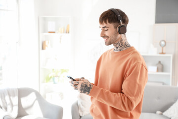 Wall Mural - Young tattooed man in headphones with mobile phone listening to music at home