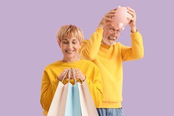 Wall Mural - Mature couple with shopping bags and piggy bank on lilac background