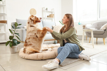 Sticker - Young woman holding paws of cute Australian Shepherd dog on pet bed at home