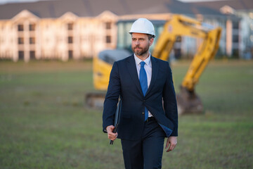 Wall Mural - Construction manager in suit and helmet at a construction site. Construction manager worker or supervisor wearing hardhat in front of house. Supervisor construction manager near excavator. Renovation.