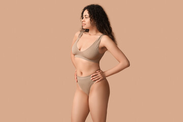 Wall Mural - Beautiful young happy African-American woman in underwear on beige background