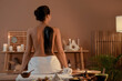 © Pixel-Shot - Young woman with mud sitting in dark spa salon, back view