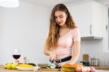 Wall Mural - Confident young woman cooking lunch in a home kitchen, cutting fresh vegetables