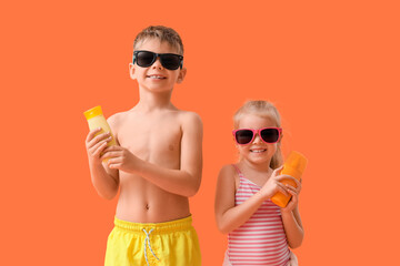 Wall Mural - Cute little children in sunglasses with sunscreen cream on orange background