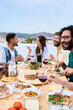 © CarlosBarquero - Vertical. Happy people around meal table with wine glasses and food celebration terrace barbecue party. Young multiracial friends enjoying laughing together lunch time on summer weekend on rooftop