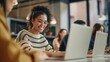 © Lens Legacy - A female professional is smiling as she works on her laptop in a busy, dynamic office environment
