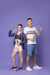 Wall Mural - Young man and woman with badminton rackets on purple background