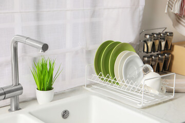 Wall Mural - Drainer with different clean dishware, glass and cup on light table near sink indoors