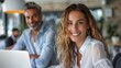 © Lens Legacy - Confident young woman smiling with a male colleague in the background at a coworking office space