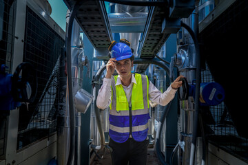 Wall Mural - An industrial worker in high-visibility gear and a blue helmet meticulously examines the intricate network of machinery. The engineer is dedicated to maintaining operational efficiency and safety.