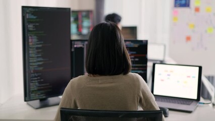 Wall Mural - an asian woman programmer is focused on coding at her dual-monitor workstation, surrounded by screen