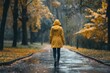 © Ева Поликарпова - A woman walks down a road wearing a bright yellow raincoat, great for use as a stock photo in travel or weather-related contexts