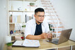 © Gatot - Asian freelancer man sitting at home office using laptop and cell phone