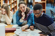 © NonVig/peopleimages.com - Library, people and studying with book, page and reading for exam, woman and man in campus of college. Students, friends and teamwork for test, information and table with research and together