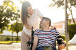 ©  Yistocking - An adult man with a disability sits in an automatic wheelchair with a young woman in a park at sunset.The woman and the man look at each other happily. Concept of support for disabled people.