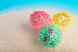© sandor - Colorful cocktail umbrellas on sea sand, blue background. Vacation concept. Summer background.