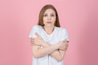© Павел Костенко - Attractive caucasian young blonde woman in casual white t-shirt hugging herself and trembling from the cold, she is frozen isolated on pink studio background.