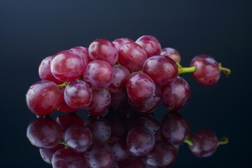 Wall Mural - Several ripe red grapes rest on a dark black table surface