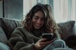 © 路加 石 - A happy young woman, sitting at home on the couch using her smartphone, smiling and looking at the screen while shopping online or working on social media apps. Social concepts, lifestyle
