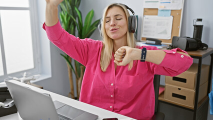 Sticker - Happy blonde woman dancing in the office with headphones, exhibiting joy and relaxation at her workplace.