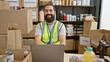 © Krakenimages.com - Handsome bearded man smiling at workplace with laptop, donation boxes, and safety vest in a well-organized storehouse.