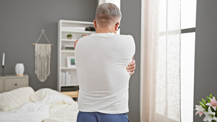 Sticker - A middle-aged man with grey hair stretches in a bright bedroom preparing for the day.