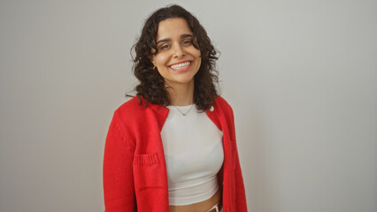 Wall Mural - Young attractive hispanic woman in a red cardigan with a white background wall, smiling confidently at the camera.