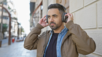 Canvas Print - Handsome bearded hispanic man listens to music with headphones on a city street.