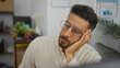 © Krakenimages.com - Young handsome hispanic man sitting in an indoor office, gazing thoughtfully with his hand on his face.