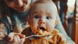 © Parintron - Intimate shot of a mother feeding her baby homemade organic apple sauce, focusing on the spoon and babyâ€™s eager mouth --ar 16:9 Job ID: c6531ac3-f806-4692-b518-b25f7f2034a1