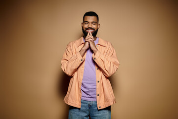 Handsome African American man in fashionable attire poses against a vibrant brown wall.