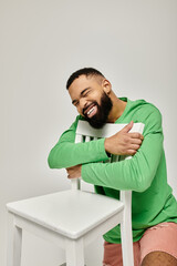 Wall Mural - A stylish African American man sits confidently on a white chair against a vibrant backdrop.