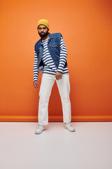 Wall Mural - Handsome African American man posing in fashionable attire against a vibrant orange backdrop.