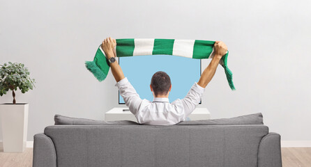 Canvas Print - Man sitting on a couch and cheering with a scarf