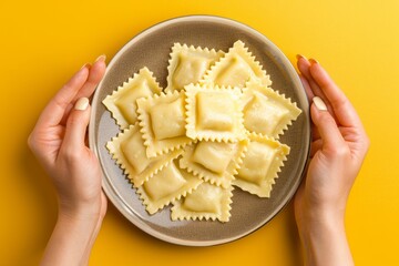 Wall Mural - Woman holding a plate full of freshly made ravioli on yellow background