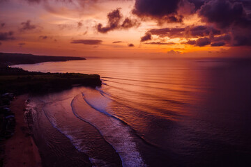 Wall Mural - Aerial view of colorful sunset and ocean with surfing waves in Bali.