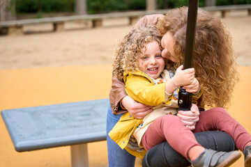 Mother and daughter are sitting on a bench, the woman is holding the child