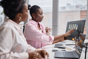Side view portrait of female developer showing online project results on computer screen at meeting in office. Multiethnic female team creating mobile app interface, UX, UI design concept, copy space