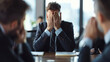 © VK Studio - A man in a suit holding his head in his hands during a high-stress business meeting, signifying frustration and pressure.