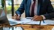© SKIMP Art - Businessman in suit signing contract on desk with laptop and documents Man taking notes, working at the office using a pen while writing Generative AI