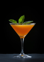 Wall Mural - Orange juice in a glass with mint leaves on a black background