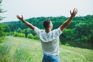 A handsome man in a white t-shirt stands in nature and breathes fresh air. Outdoor recreation. Lonely man on the background of the forest