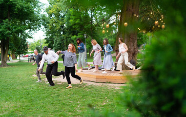 Cheerful dance party outdoors, featuring individuals of different ages enjoying the festive ambiance under illuminated string lights. They are dancing swing dance in summer city park