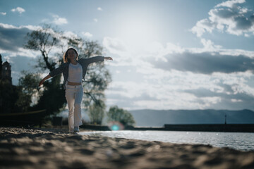 Wall Mural - Capturing a moment of pure joy, this image features a woman balancing and walking along a lake shore, evoking feelings of freedom and relaxation on a sunny day.